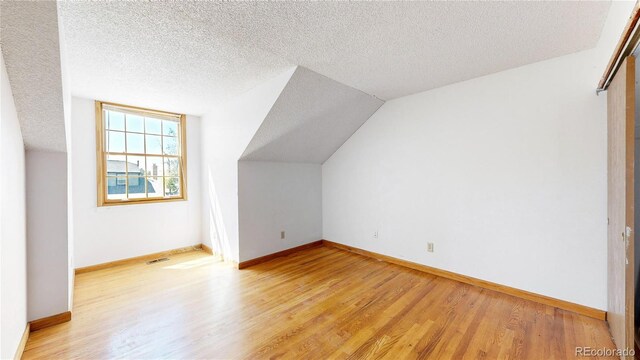 additional living space featuring lofted ceiling, light wood-type flooring, and a textured ceiling