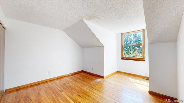 additional living space with vaulted ceiling, a textured ceiling, and light hardwood / wood-style flooring