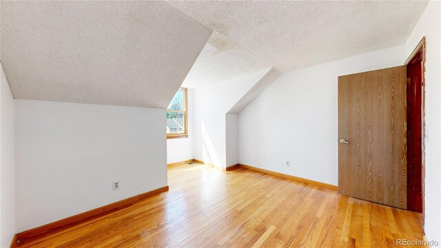 additional living space with lofted ceiling, a textured ceiling, and light hardwood / wood-style floors