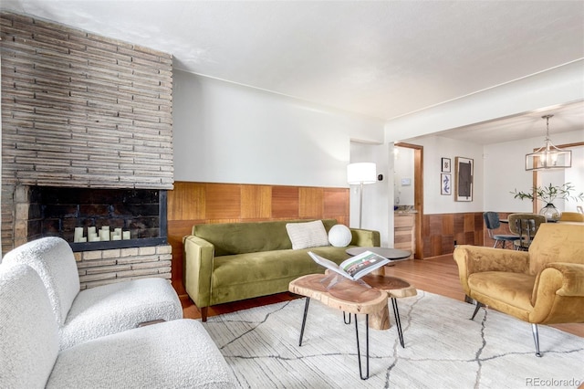 living area with wooden walls, a large fireplace, wainscoting, wood finished floors, and a notable chandelier