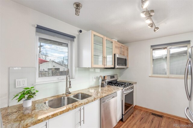 kitchen featuring visible vents, a sink, appliances with stainless steel finishes, light wood finished floors, and glass insert cabinets