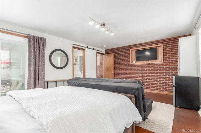 bedroom featuring ensuite bath, freestanding refrigerator, a barn door, brick wall, and rail lighting