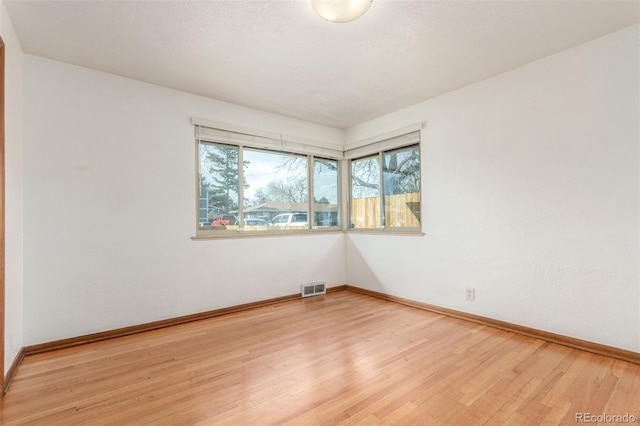 unfurnished room with visible vents, light wood-style flooring, a textured ceiling, and baseboards