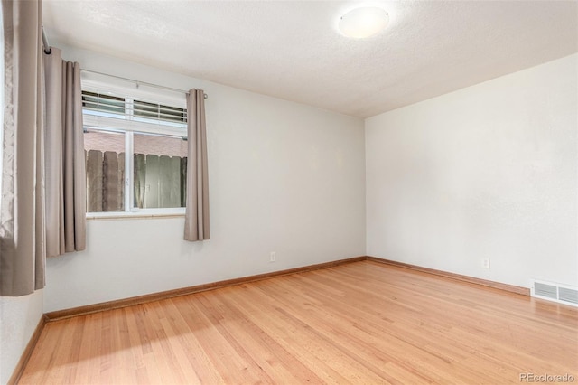 unfurnished room with a textured ceiling, wood finished floors, baseboards, and visible vents