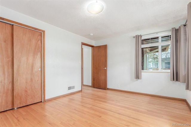 unfurnished bedroom featuring visible vents, baseboards, a closet, a textured ceiling, and light wood finished floors