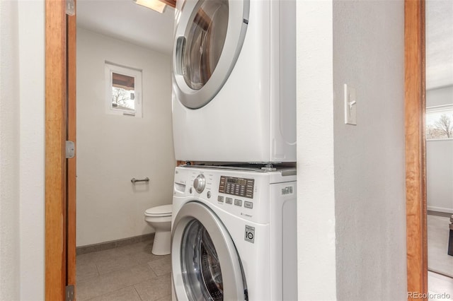 washroom featuring light tile patterned floors, laundry area, stacked washer / drying machine, and baseboards