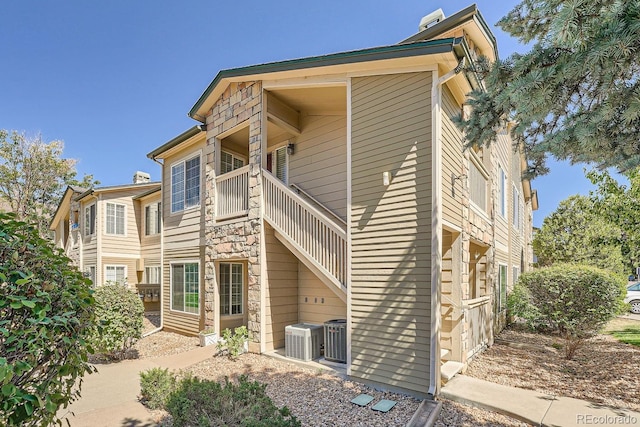 back of property with a balcony, stone siding, and cooling unit