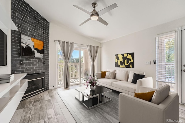 living room with vaulted ceiling, ceiling fan, light wood-type flooring, and a brick fireplace