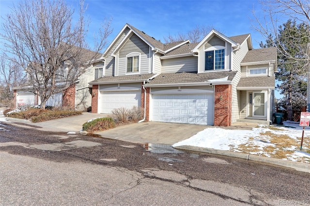 traditional-style house with a garage, concrete driveway, brick siding, and roof with shingles