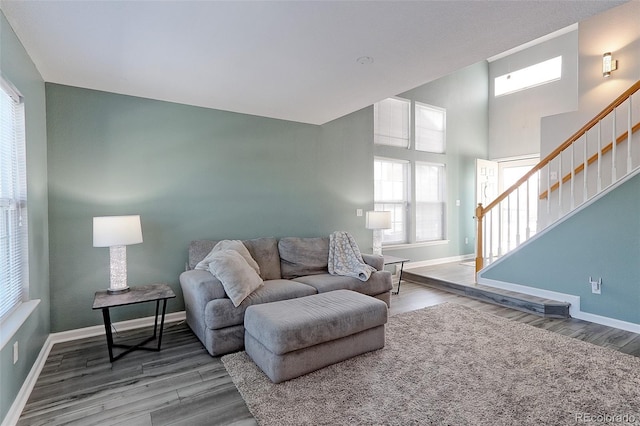 living area featuring a towering ceiling, baseboards, stairway, and wood finished floors