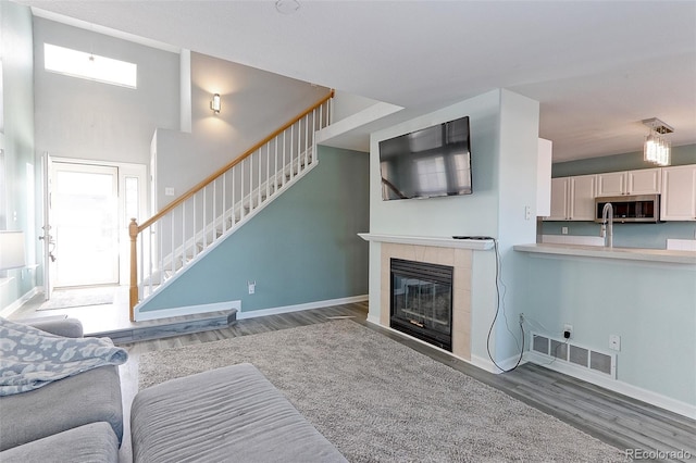 living room featuring light wood finished floors, baseboards, visible vents, stairway, and a fireplace