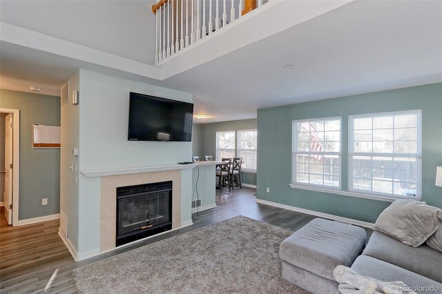 living room with dark wood-type flooring, a tile fireplace, a towering ceiling, and baseboards