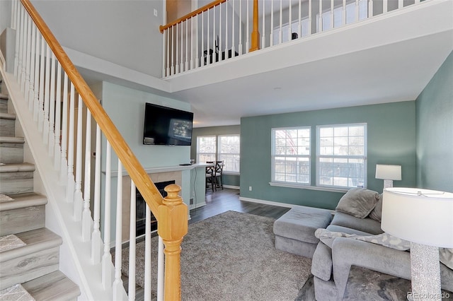 living area with a tile fireplace, wood finished floors, a towering ceiling, baseboards, and stairway