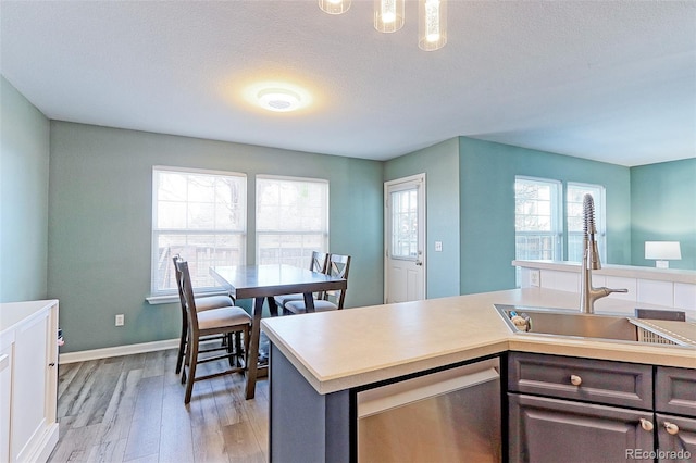 kitchen with an island with sink, light countertops, light wood-type flooring, stainless steel dishwasher, and a sink