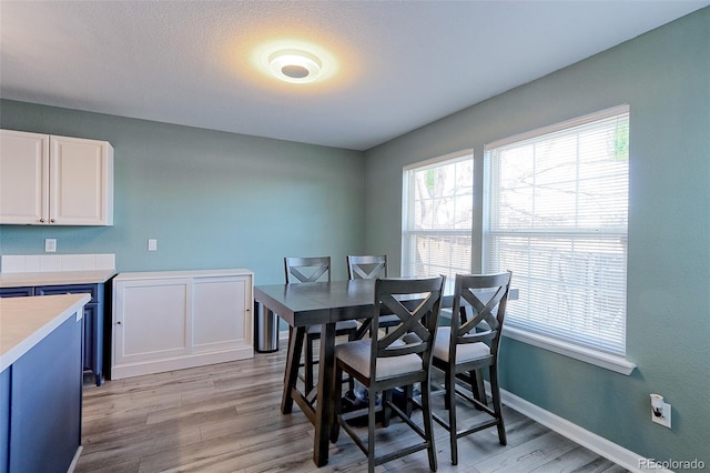 dining area with light wood-type flooring, baseboards, and a textured ceiling