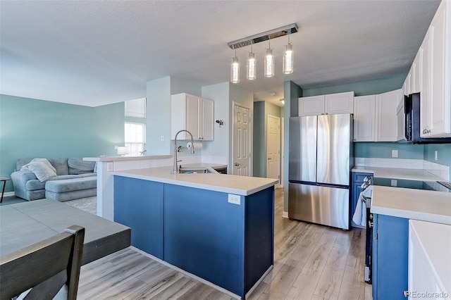 kitchen featuring stainless steel appliances, white cabinets, hanging light fixtures, light countertops, and an island with sink