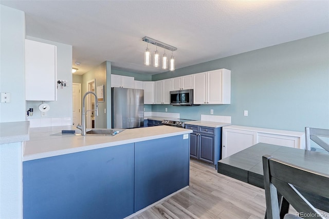 kitchen featuring appliances with stainless steel finishes, decorative light fixtures, blue cabinets, light countertops, and white cabinetry