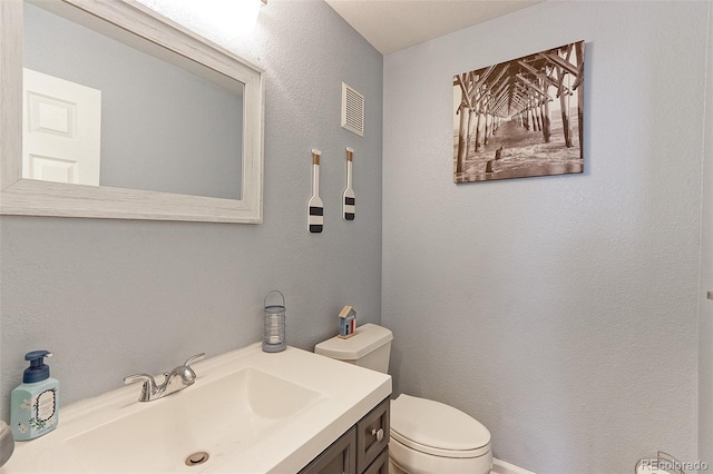 bathroom featuring toilet, a textured wall, vanity, and visible vents