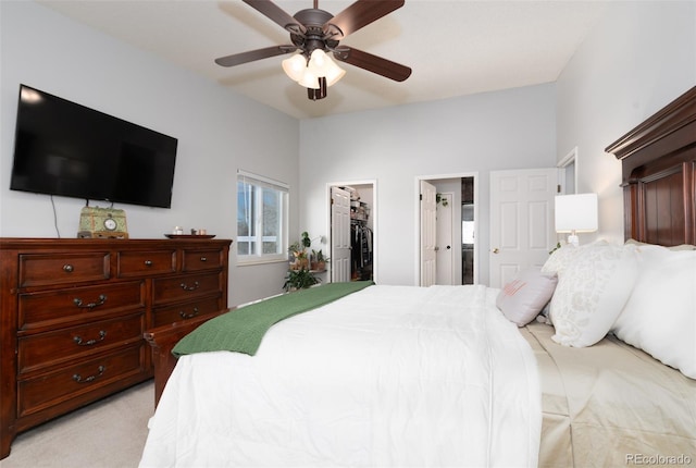 bedroom with light carpet, connected bathroom, ceiling fan, a walk in closet, and a closet