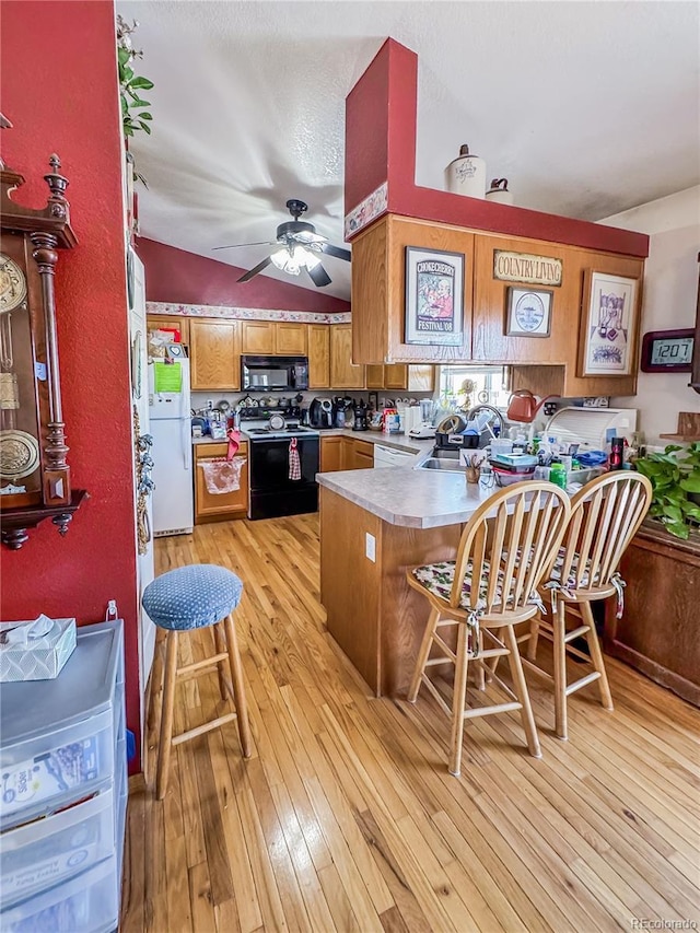 kitchen with a breakfast bar, ceiling fan, light hardwood / wood-style floors, black appliances, and kitchen peninsula