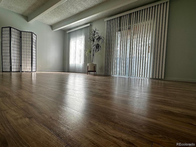 empty room with a textured ceiling, beamed ceiling, and dark hardwood / wood-style flooring