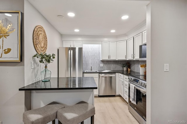 kitchen featuring stainless steel appliances, decorative backsplash, light wood-type flooring, white cabinetry, and a kitchen bar