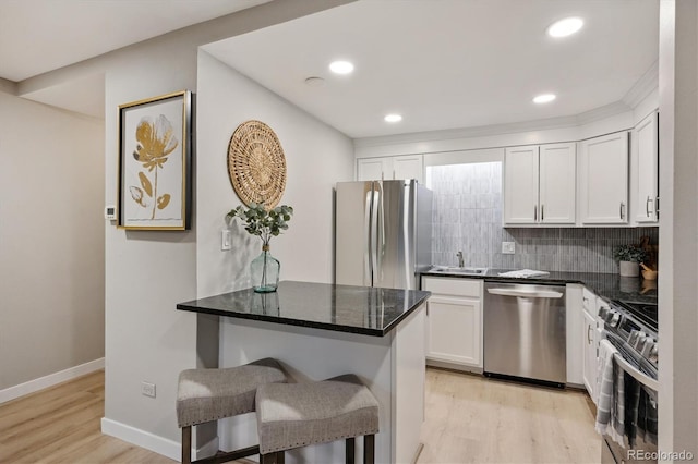 kitchen with a breakfast bar area, stainless steel appliances, light hardwood / wood-style floors, white cabinetry, and dark stone countertops