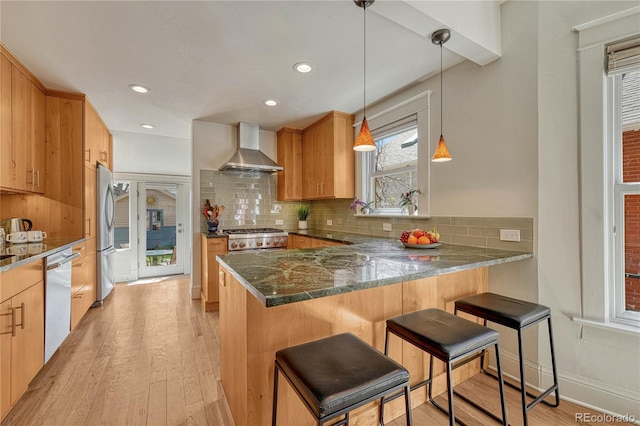kitchen with light wood-style flooring, appliances with stainless steel finishes, wall chimney range hood, and tasteful backsplash