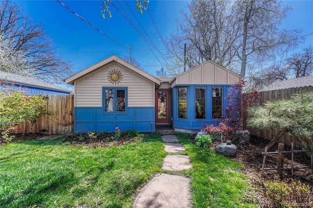view of front facade with board and batten siding, fence, and a front yard