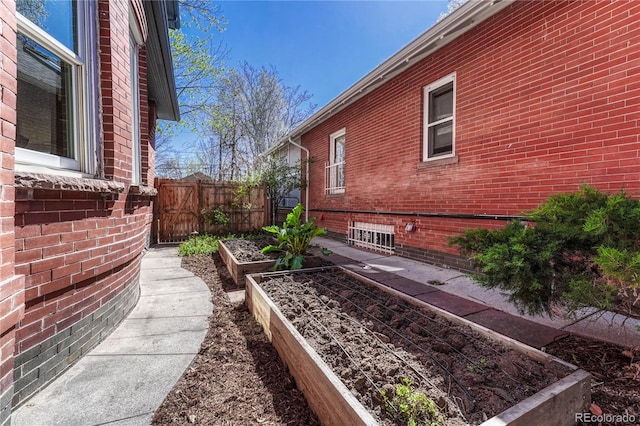 view of side of property featuring brick siding, fence, and a garden