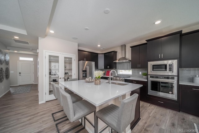 kitchen with a center island with sink, sink, appliances with stainless steel finishes, a breakfast bar area, and wall chimney exhaust hood