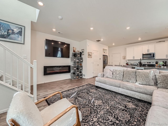17991 E 103rd Ave, Commerce City, CO 80022 - living area featuring light wood-type flooring, stairs, recessed lighting, a glass covered fireplace, and baseboards