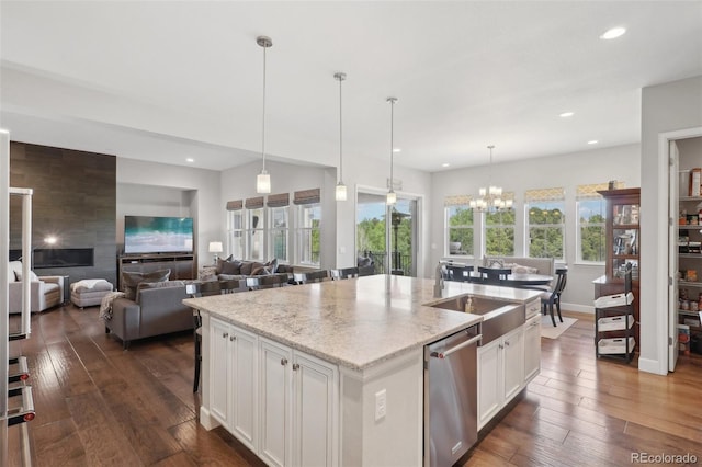 kitchen with pendant lighting, dishwasher, a kitchen island with sink, light stone countertops, and white cabinetry