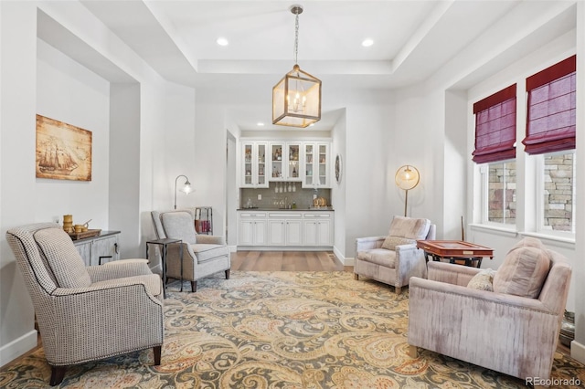 living area with indoor wet bar, an inviting chandelier, a tray ceiling, and light hardwood / wood-style flooring