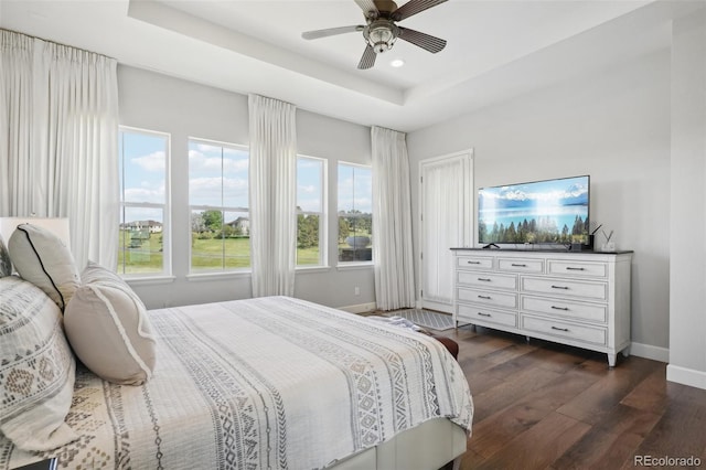 bedroom with dark hardwood / wood-style floors, ceiling fan, and a tray ceiling