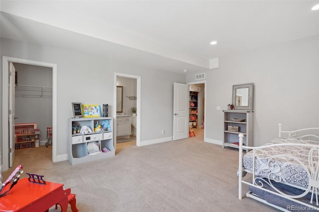 bedroom featuring connected bathroom, a spacious closet, a closet, and light colored carpet