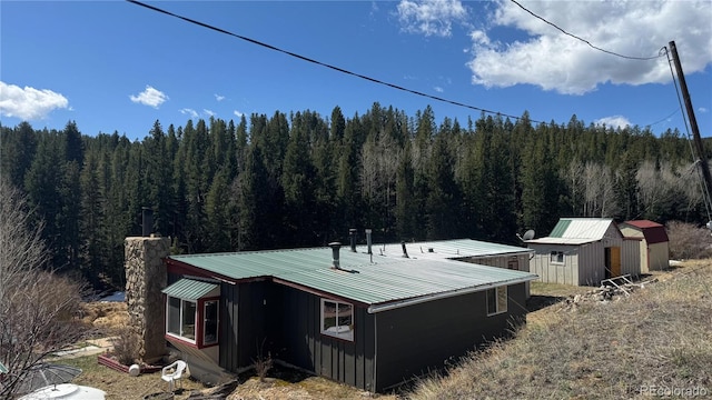 view of property exterior featuring a view of trees, an outbuilding, metal roof, and a storage unit