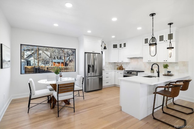 kitchen featuring decorative light fixtures, a sink, light countertops, appliances with stainless steel finishes, and glass insert cabinets