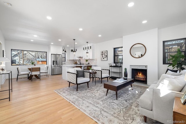 living room featuring a warm lit fireplace, light wood-style flooring, a wealth of natural light, and recessed lighting