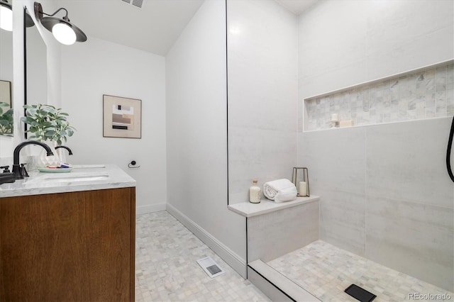 full bath with double vanity, visible vents, a sink, tiled shower, and baseboards