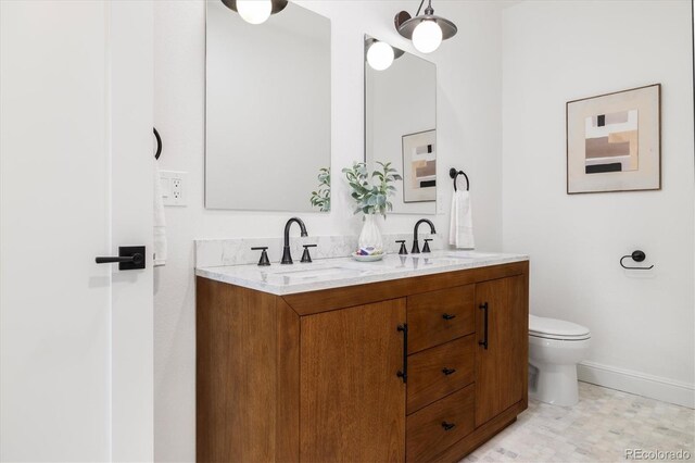 full bathroom with toilet, a sink, baseboards, and double vanity