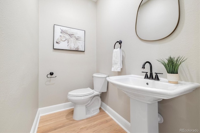 half bath with toilet, baseboards, and wood finished floors