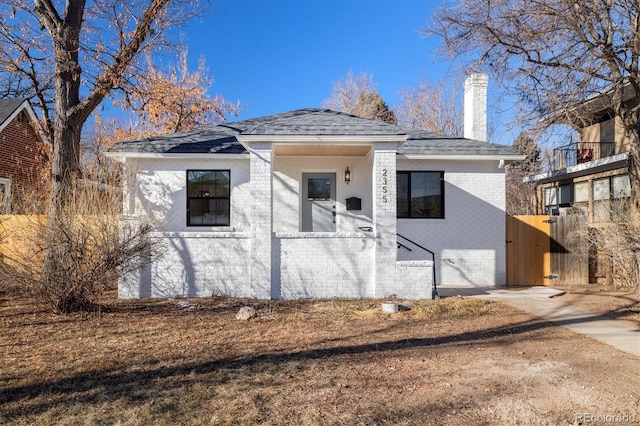 bungalow featuring brick siding, a shingled roof, fence, concrete driveway, and a chimney