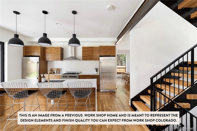 kitchen with wall chimney range hood, a breakfast bar area, pendant lighting, light wood-type flooring, and appliances with stainless steel finishes