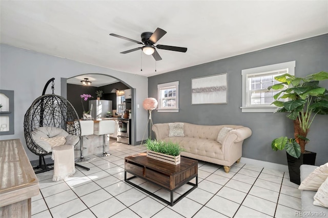 living area featuring arched walkways, light tile patterned floors, a wealth of natural light, and baseboards