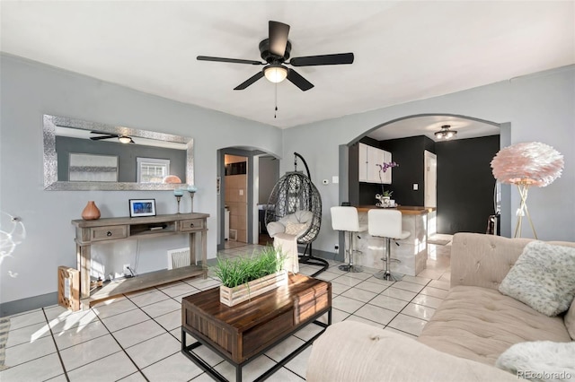 living room with a ceiling fan, arched walkways, baseboards, and light tile patterned floors