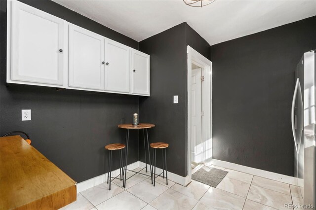 kitchen with baseboards, freestanding refrigerator, and white cabinetry