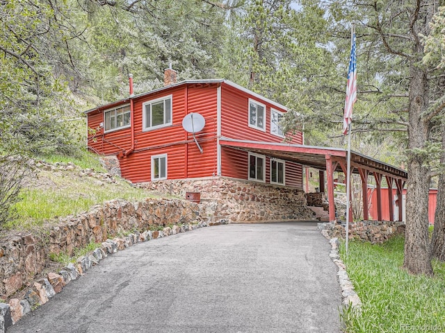 6837 S Brook Forest Rd, Evergreen, CO 80439 - chalet / cabin with asphalt driveway, a chimney, faux log siding, a carport, and view of wooded area