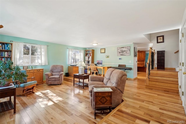 living area featuring stairs, baseboards, and light wood-style floors