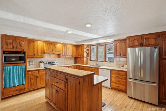 kitchen featuring decorative backsplash, appliances with stainless steel finishes, a center island, light wood-type flooring, and a sink